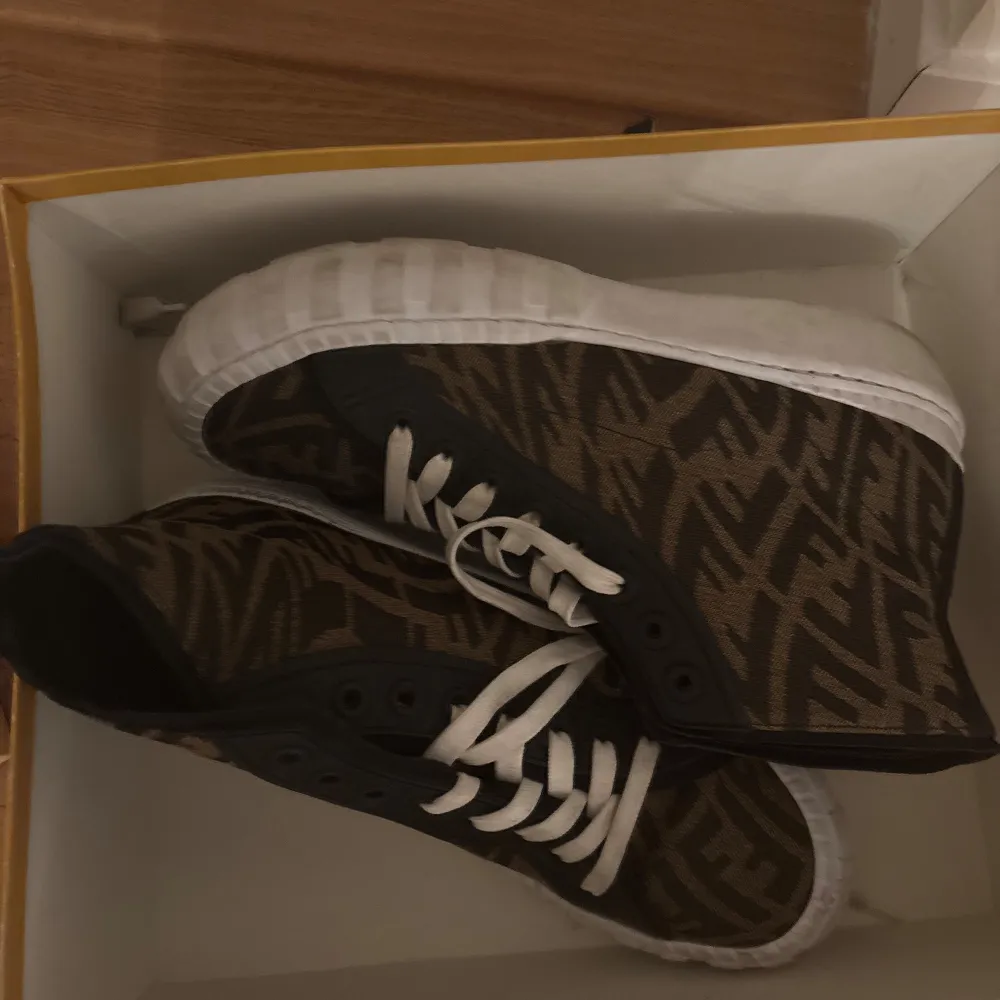 Säljer ett par snygga sneakers från Fendi i mycket bra skick. De har ett coolt mönster i brunt och svart med vita snören och sulor. Perfekta för att ge din outfit en lyxig touch. Kommer med originalförpackning och dustbag samt kvitto. Nypris ca 7000 kr. Skor.