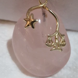 Stjärntecken Rosa hängsmycke med stjärndetalj  - Ett superfint rosa hängsmycke i form av en slät sten med en guldig stjärndetalj och små hängande dekorationer. Perfekt för att ge en magisk touch till din outfit. Passar både till vardag och fest!