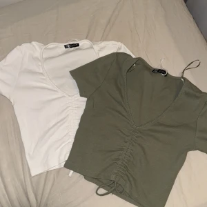 Två kortärmade toppar med knyt - Säljer två snygga toppar i vitt och olivgrönt. Båda har en v-ringad design med knytning framtill. Perfekta för sommaren och kan stylas både upp och ner beroende på tillfälle. De är i bra skick! Sitter som S