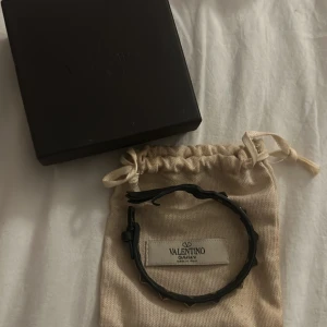 Valentino armband svart - Säljer ett snyggt svart armband från Valentino. Armbandet är välandvänt och har som man ser på bilderna släppt lite, men det funkar alldeles utmärkt att använda det. Orginalask, äkthetsbevis och påse finns med.  Köpt för 2800 kronor.  Pris kan diskuteras !!💕💕💕