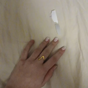 Guldfärgad vågig ring - Säljer en stilren guldfärgad ring med en vågig design. Perfekt för att ge en elegant touch till din outfit. Ringen är i mycket bra skick och passar de flesta storlekar. Perfekt accessoar för både vardag och fest!