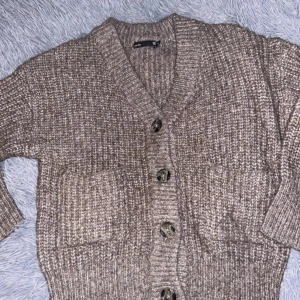 Beige stickad kofta med knappar - Mysig beige stickad kofta med stora knappar framtill. Perfekt för kyliga dagar, den har en avslappnad passform och ribbade muddar. Koftan är i bra skick.