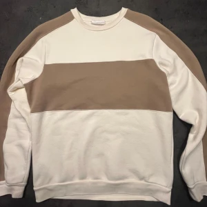 Beige och vit sweatshirt från MANGO - Säljer en snygg och bekväm sweatshirt i beige/brun och vit. Tröjan har en bred beige/brun rand över bröstet och axlarna, vilket ger den en stilren look. Perfekt för både vardag och avslappnade tillfällen. Köpte den på MANGO affär i Spanien där det grundades. Köptes för 500:-                 Den är i bra skick och redo för en ny ägare! 
