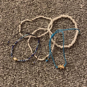 Färgglada armband i pärlor och snöre - Säljer ett set med flera armband i olika stilar. Två vita pärlarmband, ett med små pärlor och ett med större. Ett blått snörearmband med en guldig sköldpadda som detalj. Perfekt för att mixa och matcha till olika outfits (säljer alla 5 för 11kr tillsammans). 