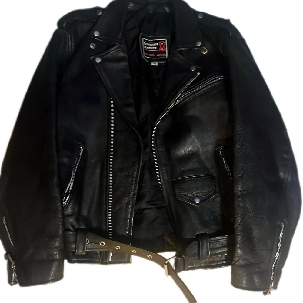 Säljer en klassisk svart skinnjacka från Genuine Leather i. Den har coola dragkedjor och ett bälte i midjan för extra stil. Perfekt för höst och vår, och ger en edgy look till vilken outfit som helst. Jackan är i mycket bra skick och redo för nya äventyr!. Jackor.