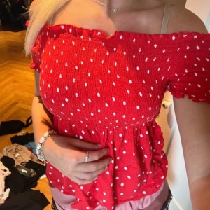 Röd offshoulder topp med prickar - Säljer en superfin röd offshoulder topp med vita prickar. Den har en smockad överdel som ger en skön och stretchig passform. Perfekt för sommardagar eller en festlig kväll. Toppen är i mycket bra skick och redo för nya äventyr! 🌟