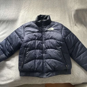 Mörkblå pufferjacka North Face - Säljer en snygg och varm mörkblå pufferjacka från The North Face i storlek M. Jackan har en dragkedja framtill och två praktiska fickor med dragkedjor. Perfekt för kalla vinterdagar! Nypris är 2400kr från Zalando, så väldigt generöst pris! Går ändå att diskutera pris.