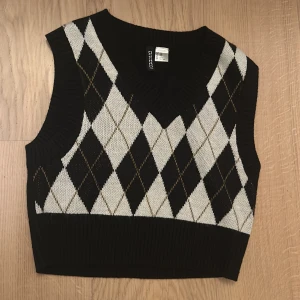 Svart och vit rutig stickad väst  - Säljer en snygg stickad väst från Divided i svart och vitt med ett klassiskt rutmönster. Västen har en v-ringad design och är perfekt för lager-på-lager under hösten. Den är i mycket bra skick och är sparsamt använd 💗💗