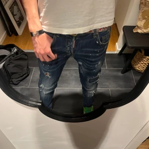 DISQUARED2 JINZZ - Säljer ett par mörkblå Disquared2 jeans som är bästa jeansen i gamet för grabbarna❤️⭐️med coola slitningar och färgstänk. De har en normal passform och är perfekta för en avslappnad stil. Jeansen har en klassisk femficksdesign och är i bra skick. Perfekta för både vardag och fest!⭐️❤️
