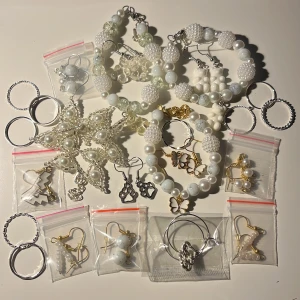 Samling av 24 smycken med pärlor och ringar - Säljer en vacker samling av smycken som inkluderar flera armband och örhängen med vita pärlor och detaljer i guld och silver. Perfekt för att ge en elegant touch till din outfit. Inkluderar även flera ringar i olika stilar. Passar bra till festliga tillfällen eller som en fin present.