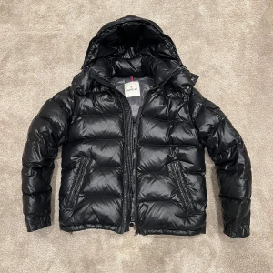 Svart Moncler Maya - Säljer en snygg och trendig svart Moncler Maya i mycket bra skick. Jackan är perfekt för vintern med sitt quiltade mönster och långa ärmar. Den har en praktisk dragkedja och en mysig huva för extra värme. Perfekt för kalla dagar! Nypris: 17000kr. Kommer ej med något tillbehör, men äkthetsbevis finns. Nästintill inga defekter, men kom PM för detaljer. Lite äldre modell. Den är storlek 3 vilket motsvarar ungefär medium. Garanterat äkta☑️Fraktar samma dag som beställning på köparens bekostnad🤝