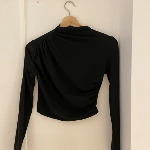Svart långärmad topp - Snygg svart långärmad topp i croppad modell. Perfekt för både vardag och fest! Den har en stilren design som gör den lätt att matcha med olika outfits. Toppen är i bra skick och redo för en ny ägare. Passar perfekt till höst- och vårgarderoben.