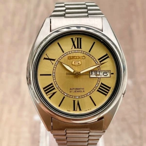 Seiko 5 automatisk klocka - Säljer en vintage  Seiko 5 automatisk klocka från 2000 talet, i mycket bra skick. Den har en stilren guldfärgad urtavla med romerska siffror och dag/datumvisning(obs dag funktionen funkar inte). Boetten och armbandet är i rostfritt stål, vilket ger en klassisk och tidlös design. Skriv vid frågor🫶