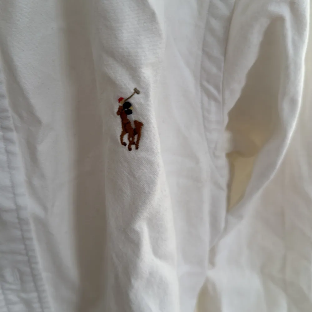 Säljer en klassisk vit skjorta från Ralph Lauren i slim fit. Skjortan är i stretchigt oxford-tyg och har långa ärmar. Den har knappar framtill och en broderad logga på bröstet. Perfekt för både vardag och fest! 🕺. Skjortor.