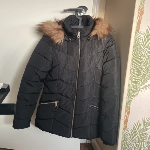 Svart vinterjacka från KappAhl - Säljer en jättefin svart vinterjacka från KappAhl i storlek 164. Jackan har fuskpäls på huvan och guldiga dragkedjor på fickorna. Perfekt för kalla vinterdagar! 💕