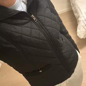 Svart quiltad jacka från ONLY - Säljer en snygg svart quiltad jacka från ONLY i storlek M. Jackan har dragkedja och knappar på fickorna, perfekt för höst och vår. Den är i mycket bra skick och passar till både vardag och fest. Superbekväm och stilren!