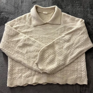 Beige stickad tröja med krage - Mysig beige stickad tröja med en klassisk krage och ett snyggt mönster. Tröjan har långa ärmar och ribbade kanter, använt någon enstaka gång. Köpt för 499kr