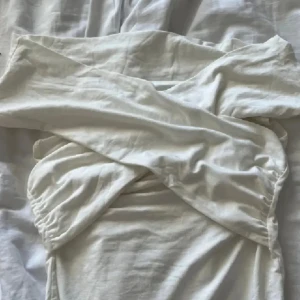 Vit offshoulder topp - Säljer en superfin vit offshoulder topp i mjukt material. Perfekt för sommarens alla fester eller en mysig midsommar. Klänningen har en elegant omlott-design som ger en snygg passform. Den är i bra skick och redo för nya äventyr!