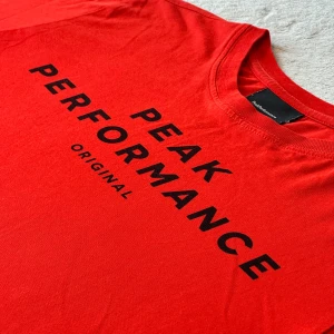 Röd t-shirt från Peak Performance - Säljer en snygg röd t-shirt från Peak Performance. Loggan är tryckt i svart på bröstet. Passar perfekt till jeans etc. Fint skick! 
