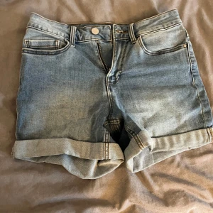 Blå jeansshorts från Vila - Snygga blå jeansshorts från Vila i en klassisk design med upprullade benslut. Perfekta för en avslappnad sommarlook. De har fem fickor och en knappgylf.