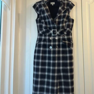 Rutig klänning med bälte - Snygg rutig klänning med v-ringad design och knappar framtill. Den har ett bälte i midjan som ger en fin silhuett. Perfekt för en stilren look.