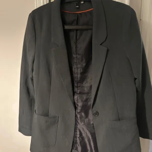 Kavaj  - Grå figursydd kavaj med i knapp och fickor framtill. Märker är från H&M.