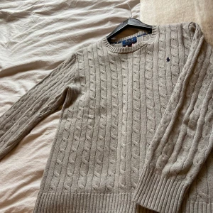 Grå kabelstickad tröja från Ralph Lauren - Säljer en stilren grå kabelstickad tröja från Ralph Lauren. Tröjan har en klassisk design med rund hals och långa ärmar. Perfekt för kyligare dagar och ger en tidlös look. 🧶
