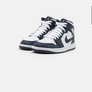 Air jordan 1 mid- white/metallic gol/obsidian - Air jordan skor i storlek 40.5. Skorna är använda men i välbevarat skick, har knappt någon skråma. Skorna skickas med två par skosnören, vita och mörkblå. Köpta för 1500kr. 
