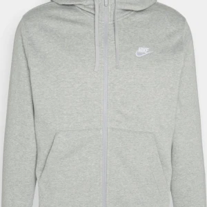 Grå Nike hoodie  - Säljer en stilren grå hoodie från Nike med dragkedja och justerbar huva. Perfekt för en avslappnad look. Den har en liten Nike-logga på bröstet och praktiska fickor framtill.Koftan är helt ny. Säljer den för att den passade inte.