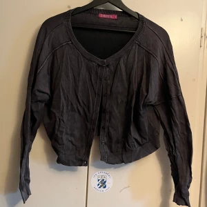 Croppad kofta från Indiska - Säljer en mörkgrå croppad kofta från Indiska i 100% bomull. Koftan har långa ärmar och knappar framtill. Perfekt för en avslappnad stil. Har använt flera gånger men den har inga defekter, dock i bilden är den skrynklig från dålig förvaring men det är inget som en tvätt inte kan lösa ☺️Framsidan ser längre ut en baksidan men det är bara på grund av hur den är hängd på galjen, om den hänger vanligt så åker den av