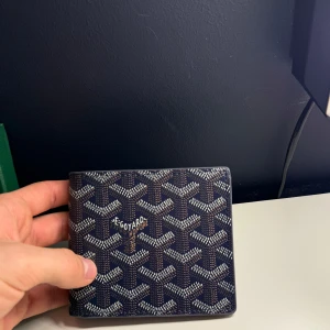 Mönstrad plånbok  - Snygg plånbok från Go**rd med ett ikoniskt mönster i blått och vitt. Plånboken har flera kortfack och en stilren design som passar perfekt i fickan. Den kommer i en elegant grön förpackning.