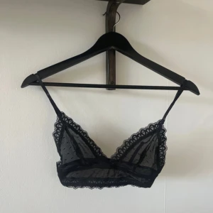 Svart spets bralette - Snygg svart bralette i spets med prickigt mönster. Den har justerbara axelband och en dekorativ kant. Perfekt för att lägga till en touch av elegans till din outfit.