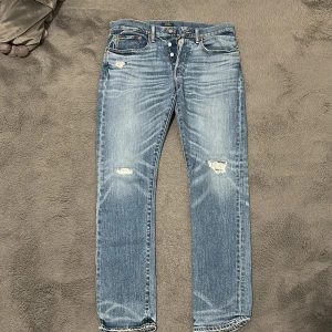 Ralph Lauren Jeans - Snygga blå jeansbyxor med slitningar på låren och knäna. De har en klassisk femficksdesign och knappar i gylfen. Perfekta för en avslappnad stil. Storlek 32/32, använda 3/4 gånger