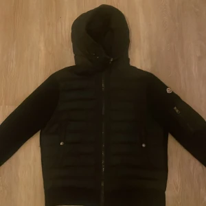 Moncler Cardigan  - Jag säljer min Moncler cardigan som jag använt i ungefär ett år. Den är i väldigt bra skick och passar perfekt både för varmare väder och kallare dagar. Jackan är mångsidig och funkar både vid finare tillfällen och för vardaglig användning. Moncler-märket syns på varje metallbit, och jackan har även QR Scan och NFC Scan vid sidan för extra autenticitet. Har du frågor eller vill ha fler bilder, tveka inte att höra av dig!