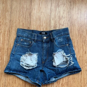 Blå jeansshorts med slitningar - Snygga blå jeansshorts från Bikbok med coola slitningar på framsidan. De har en klassisk femficksdesign och knappgylf. Perfekta för en avslappnad stil.