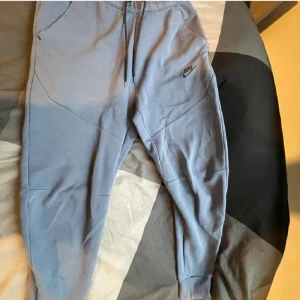  mjukisbyxor från Nike - Säljer ett par grå mjukisbyxor från Nike med dragsko i midjan och sidofickor. Byxorna har en avslappnad passform och är perfekta för en bekväm stil. Nike-loggan är broderad på ena benet.