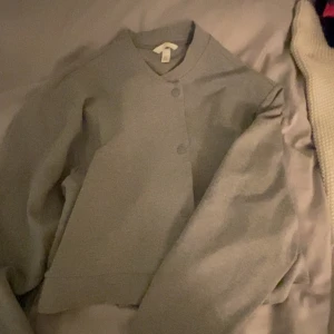 Dressad kofta - Snygg grå dressad kofta med en stilren design. Jackan har en enkel knäppning framtill och en klassisk krage. Perfekt för en cool och avslappnad look.