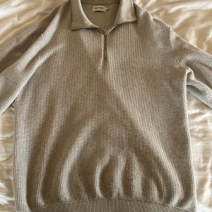 Grå stickad tröja från east west - Snygg grå stickad tröja från east west med dragkedja vid halsen. Perfekt för kyligare dagar med sin ribbade struktur och långa ärmar. En stilren och bekväm tröja som passar till många tillfällen.