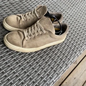 Beige sneakers i mocka - Snygga beige sneakers i mocka med snörning. Perfekta för en avslappnad stil. De har en klassisk design med rund tå och en ljus sula.