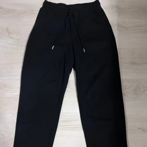 Svarta mjukisbyxor med snörning - Säljer ett par svarta mjukisbyxor med elastisk midja och snörning. Perfekta för en avslappnad stil och bekväma att bära. Byxorna har en enkel design utan mönster eller extra detaljer.