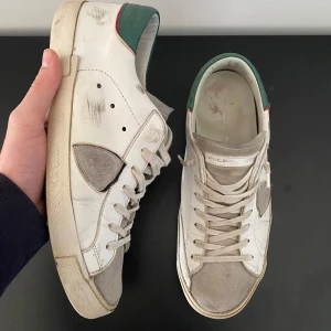 Philippe model skor - Snygga vita sneakers från Philippe Model med gröna och röda detaljer. Skorna har snörning och en grön sula. Perfekta för en stilren look. Storlek 42 men sitter som 43. Skick 8/10. Box och dustbag saknas. Pris kan diskuteras vid snabb affär. Skriv för fler frågor eller bilder. 🚨BYTEN ÄR INTRESSANTA!🚨Liten defekt på sulan syns på sista bilden. Går lätt att laga hos en skomakare