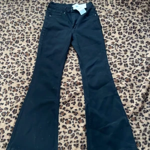 Svarta bootcut byxor - Snygga svarta bootcut byxor med hög midja. Perfekta för en stilren look. Byxorna har en klassisk design med dragkedja och knappar framtill. 