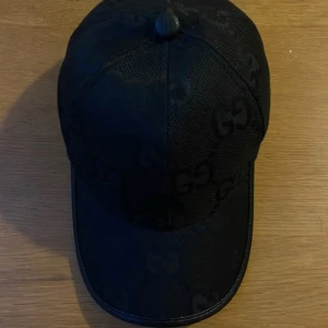 Svart keps  - Snygg svart keps med diskret GG-mönster. Perfekt för en stilren look. Kepsen har en klassisk design med rundad skärm. Fraktar inom 24 timmar. 