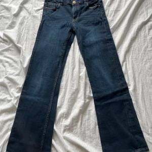Mörkblå jeans från Polarn O. Pyret - Snygga mörkblå jeans från Polarn O. Pyret med klassisk femficksdesign och knappgylf. Perfekta för en avslappnad stil med en touch av elegans. Märkeslappen i läder ger en extra detalj. 