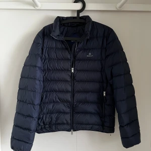 Mörkblå pufferjacka från GANT - Säljer en snygg mörkblå pufferjacka från GANT. erfekt för kyligare dagar. Nypris ligger på ca 2600 kr den är i mycket bra skick syns inget på att den är använd skriv i dm om ni har några frågor.