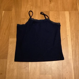 Mörkblått linne från Kappahl - Säljer ett svart linne från Kappahl med spetsdetaljer upptill. Linnet har smala axelband och är perfekt för varma dagar eller som ett lager under andra plagg.