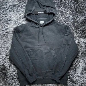 Svart hoodie från C.P. Company - Snygg svart hoodie från C.P. Company med klassisk design och huva med dragsko.  Bra skick 8/10| storlek L men sitter bra som M|