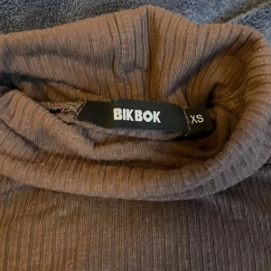 Brun långärmad tröja från Bik Bok - Säljer en stilren brun långärmad tröja från Bik Bok i storlek XS. Tröjan har en ribbad textur och långa ärmar, perfekt för kyligare dagar. Den är både bekväm och trendig, idealisk för lager-på-lager-stil. Hör av dig vid intresse!