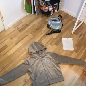 Beige velour hoodie med byxor - Säljer en mysig beige velour hoodie med matchande byxor. Hoodien har dragkedja och texten 'Love' i glittriga stenar på bröstet. Byxorna har en elastisk midja och samma 'Love'-detalj. Perfekt för en avslappnad stil.