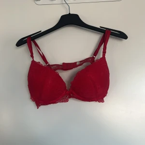 Röd spets-BH med snörning - Snygg röd BH i spets med dekorativ snörning framtill. Den har justerbara axelband och en elegant design som ger en feminin touch. Perfekt för att känna sig extra fin. Har klippt av lappen men har för mig att den är i storlek 75 C